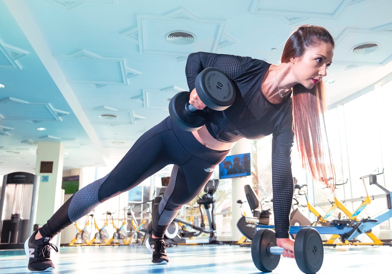 about-01 Woman performing a plank row with dumbbells in a bright Dubai gym.