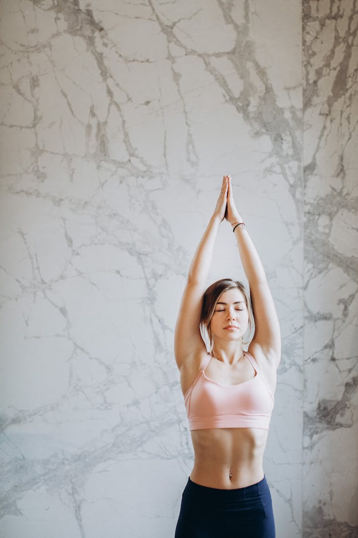 our-services-2 Young woman performing upward salute yoga pose indoors with marble background.