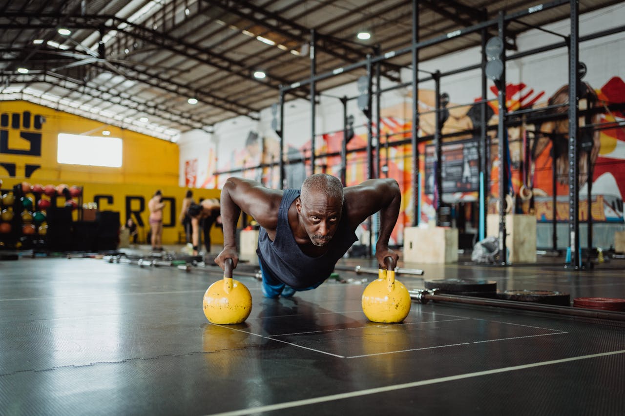 hero-img-02 Focused man performing push-ups with kettlebells in a vibrant gym setting.